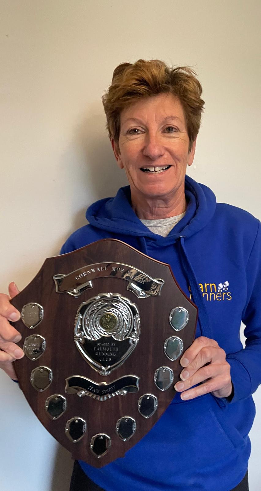 Janet holding the Team Spirit Award shield, wearing a blue Carn Runners hoodie.